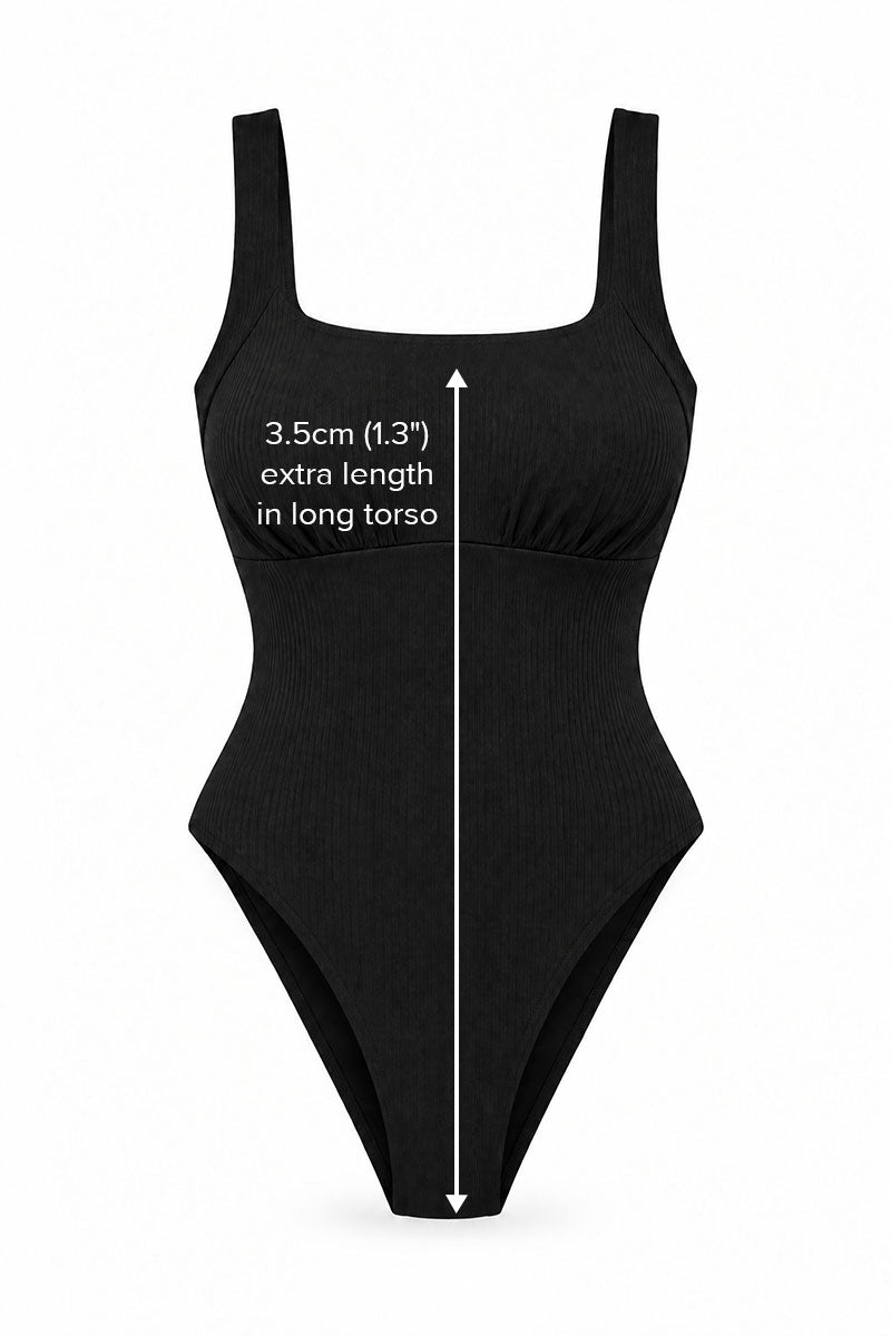 Black one-piece swimsuit with white text and measurement arrows indicating an extra 3.5cm (1.3") length in the long torso.