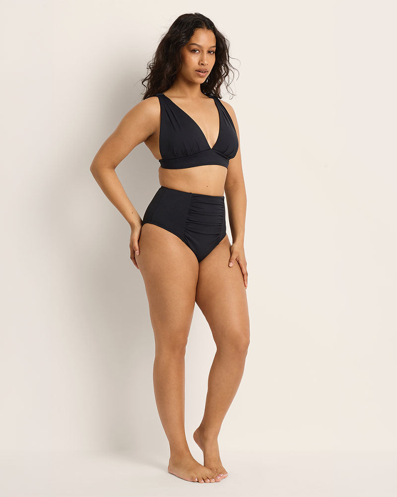 Woman wearing a full coverage, supportive bust, black bikini set on a plain background. High waist bikini bottoms.