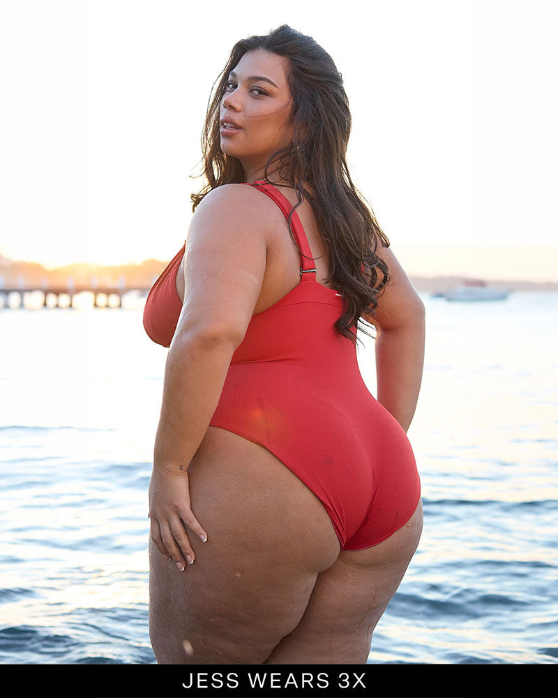 Woman wearing a full coverage, supportive bust red one piece swimsuit by a body of water with 'JESS WEARS 3X' text.