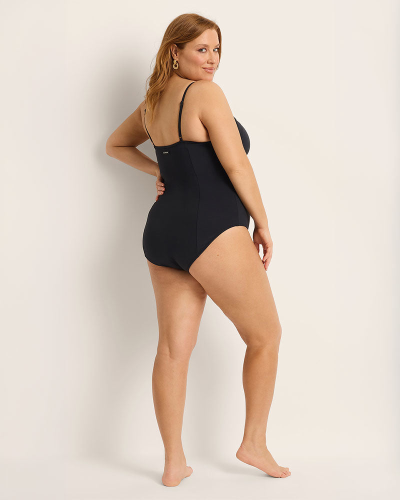 Woman wearing a full coverage black one-piece swimsuit against a plain background