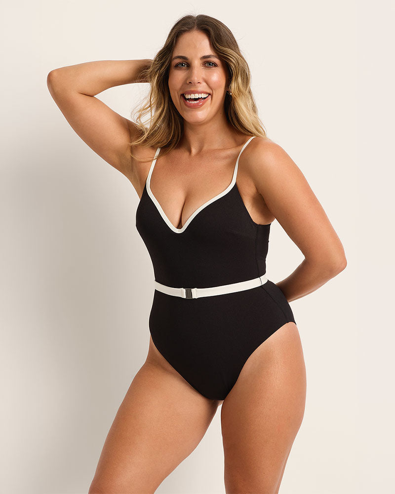 Woman wearing a supportive black swimsuit with white trim against a plain background