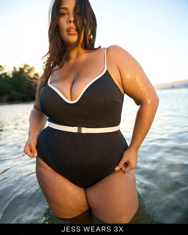 Woman in a black and white full coverage swimsuit standing in water with a scenic background