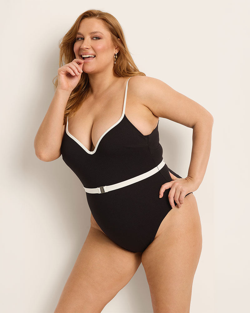 Woman wearing a supportive black swimsuit with white trim against a plain background