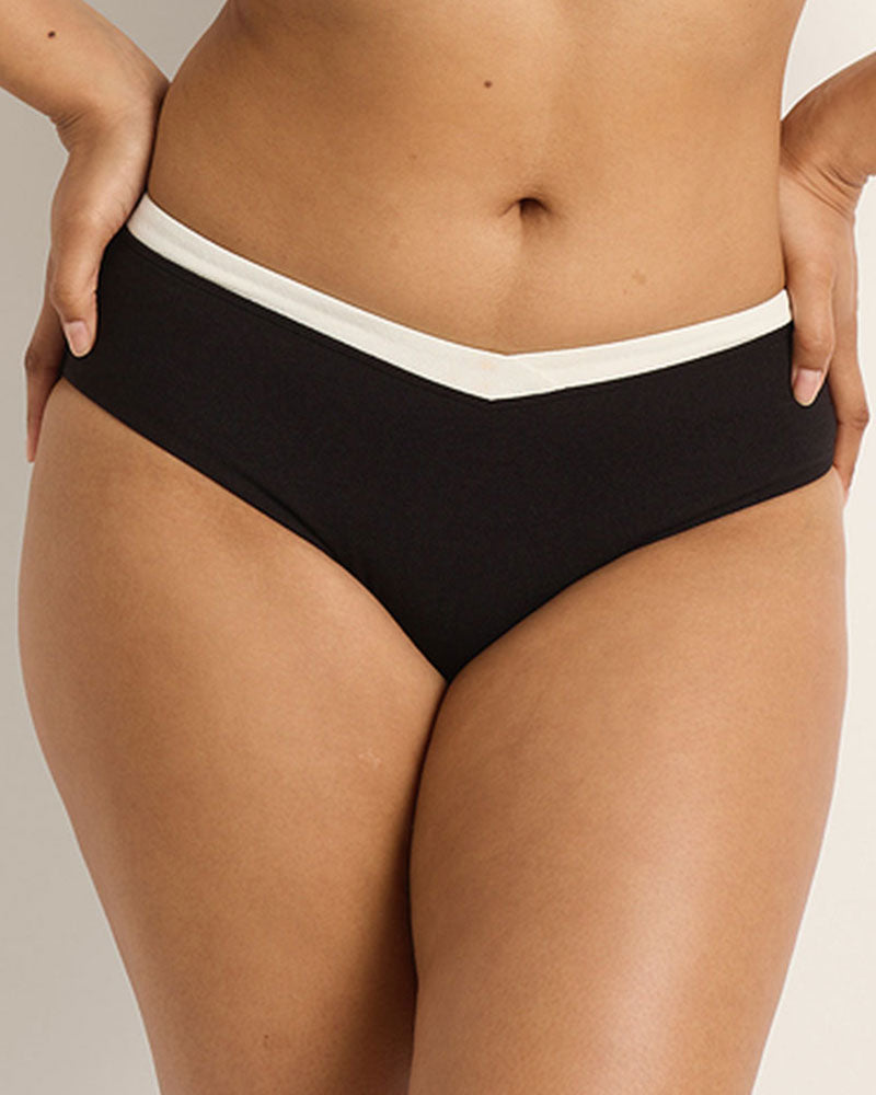 A woman wearing a mid rise black bikini bottom with white waistband on a neutral background