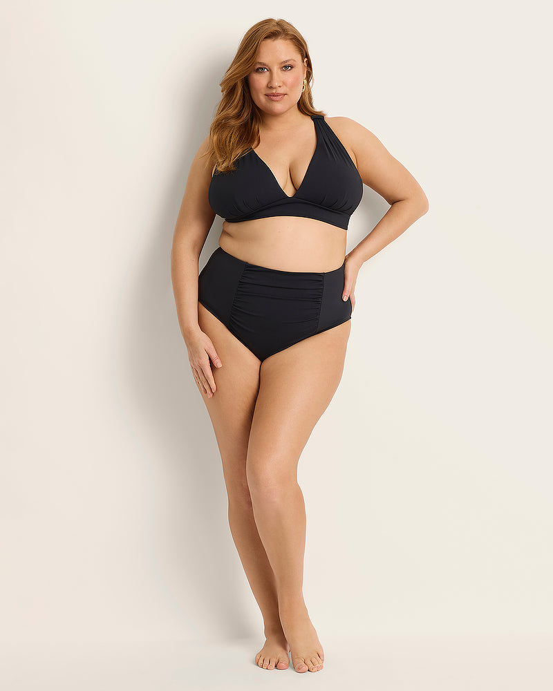 Woman wearing a Fearless supportive bust and high waist black bikini against a plain background.