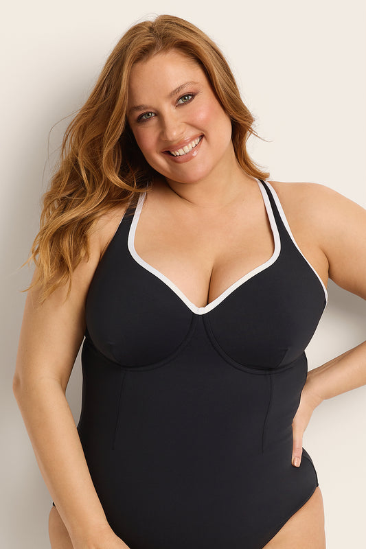 Woman wearing a supportive bust black and white swimsuit with white trim against a plain background.