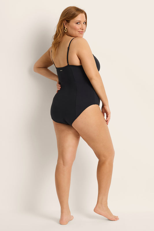 Woman wearing a full coverage black one-piece swimsuit against a plain background