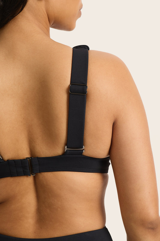 A close-up of a woman's back highlights the adjustable straps and clasp of the Fearless au All Day Bikini Top-Matte Black, designed for supportive swimwear, set against a neutral background.