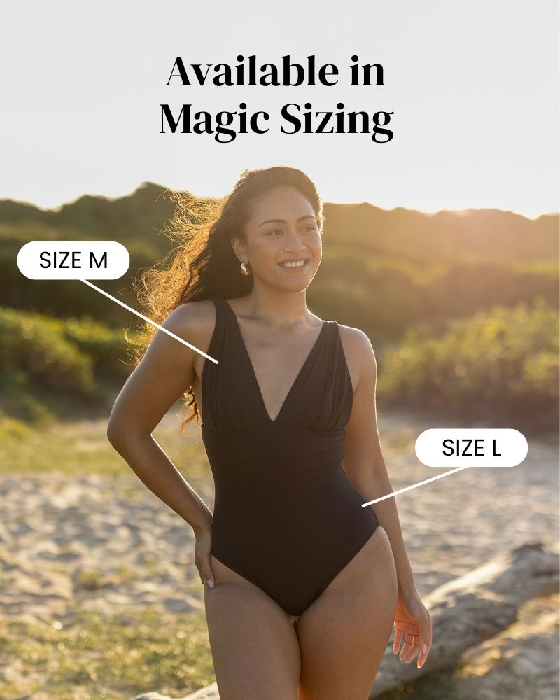 A woman stands on a sandy beach at sunset wearing a black swimsuit. Text reads “Available in Magic Sizing.” Labels point to the swimsuit, indicating it fits as both size M and size L.