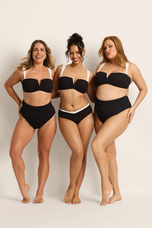 Three women of various body types smile confidently in matching black and white swimsuits, capturing the spirit of self-love—a great fit for gifting the Fearless Gift Card from Fearless, set against a simple light background.