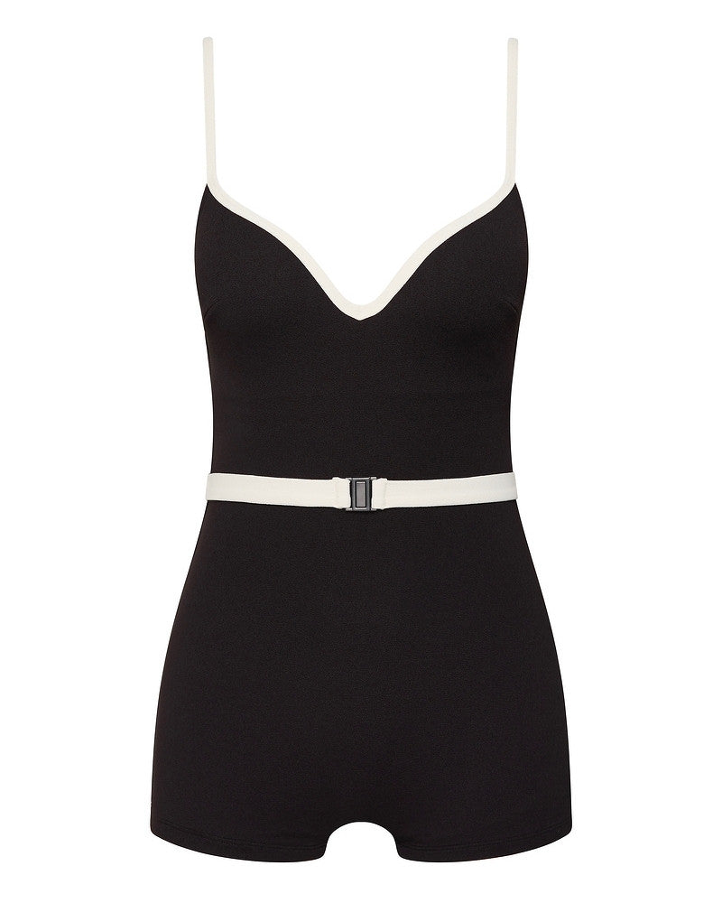 A black one-piece romper with a deep V-neckline, thin white shoulder straps, and a white belt with a rectangular buckle at the waist. The outfit has short legs and a fitted silhouette.