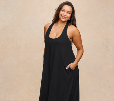 A woman modeling a black halter-neck maxi dress with side pockets, standing against a textured beige studio backdrop.