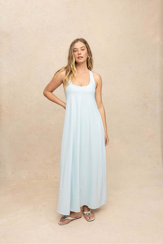 A woman modeling a light blue sleeveless maxi dress against a textured beige studio backdrop.