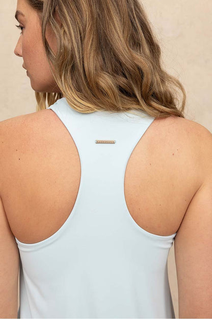 A woman shown from the back wearing a light blue racerback tank top with a small gold bar detail at the center of the neck, set against a neutral beige background.