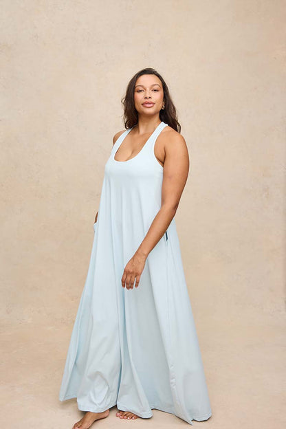 A woman modeling a light blue sleeveless maxi dress against a textured beige studio backdrop.