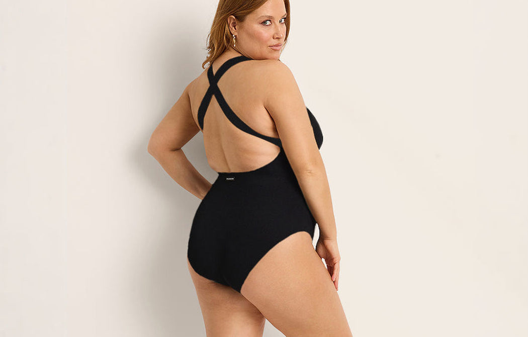 Woman wearing a black swimsuit with criss-cross straps on a beige background