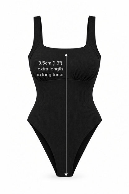 Black one-piece swimsuit with white text and measurement arrows indicating an extra 3.5cm (1.3") length in the long torso.