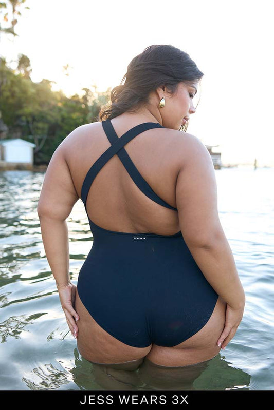 Woman wearing a black swimsuit standing in water with trees in the background