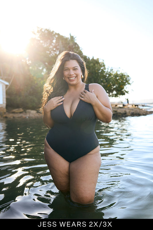 Woman in a black swimsuit standing in water with trees and sunlight in the background