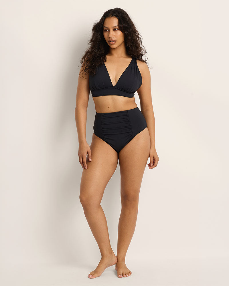 Woman wearing a Fearless supportive bust and high waist black bikini against a plain background.