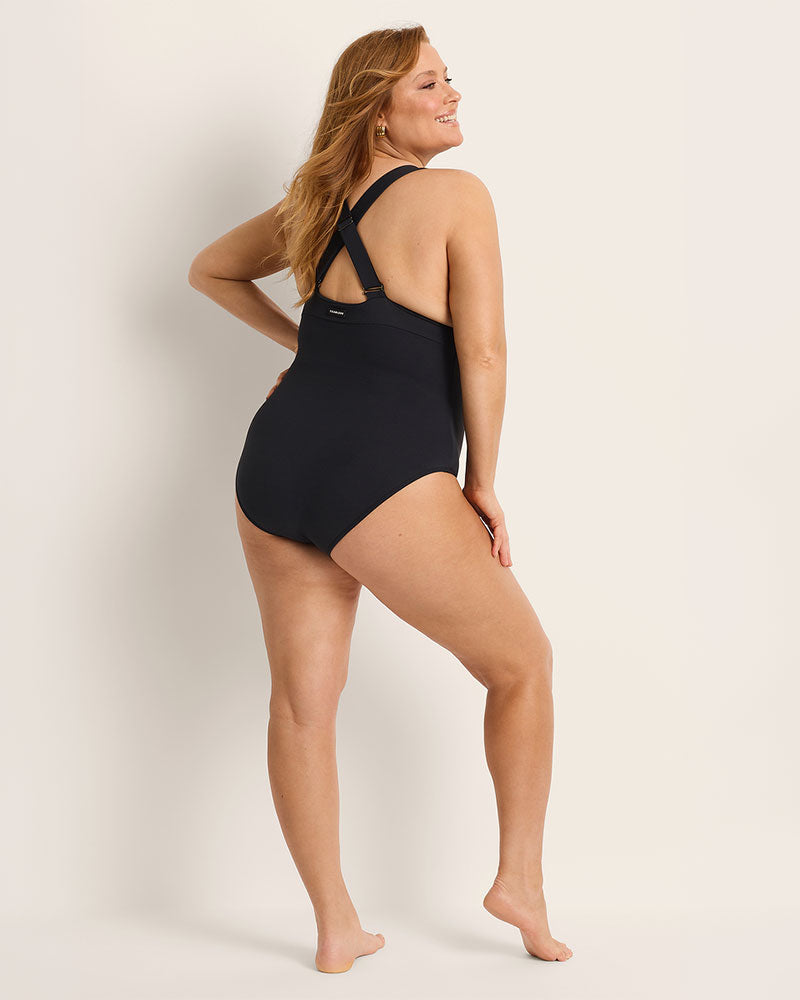 Woman wearing a black supportive bust one-piece swimsuit against a plain background