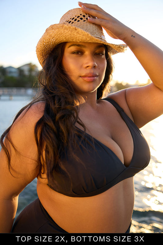 Woman in a black bikini and straw hat by a body of water