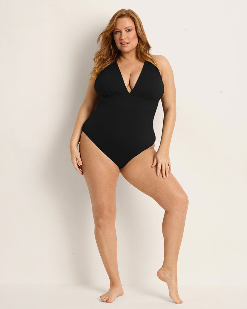 Woman wearing a supportive bust black one-piece swimsuit against a plain background.