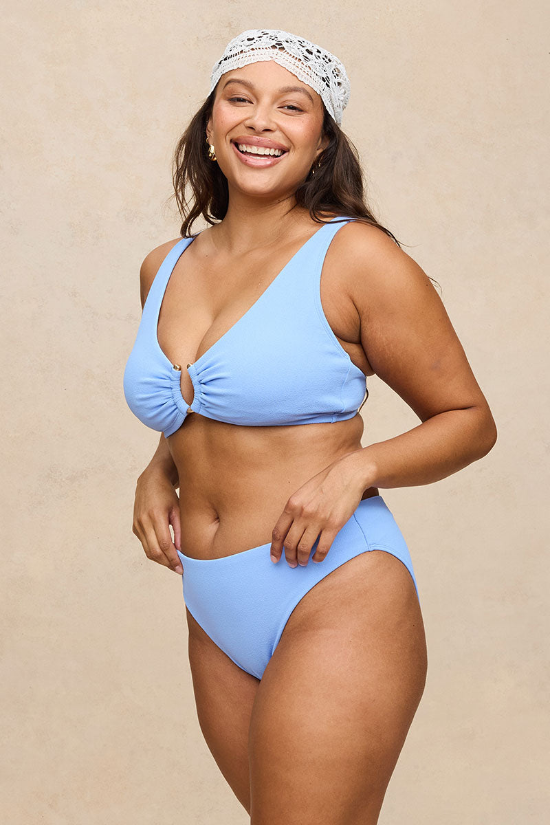 A woman modeling a light blue two-piece bikini with a front keyhole detail on the top, paired with matching high-cut bottoms, against a neutral beige background.