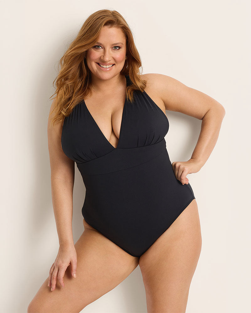 Woman wearing a supportive bust black one-piece swimsuit against a plain background.