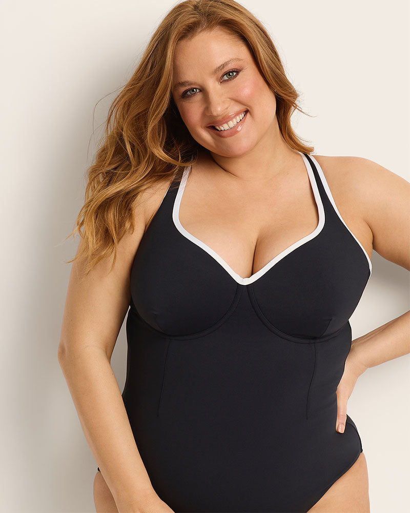 Woman wearing a supportive bust black and white swimsuit with white trim against a plain background.