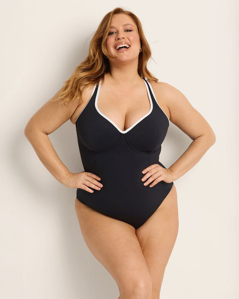 Woman wearing a supportive bust black and white swimsuit with white trim against a plain background.
