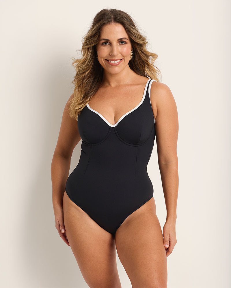Woman wearing a supportive bust black and white swimsuit with white trim against a plain background.