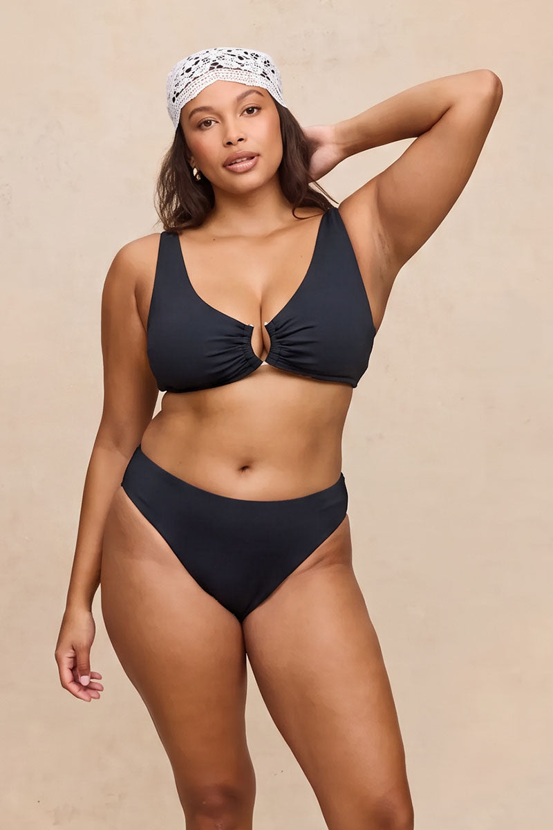 A woman modeling a two-piece bikini set in black color, featuring a ruched keyhole front on the top and high-waisted bottoms, set against a solid beige background.