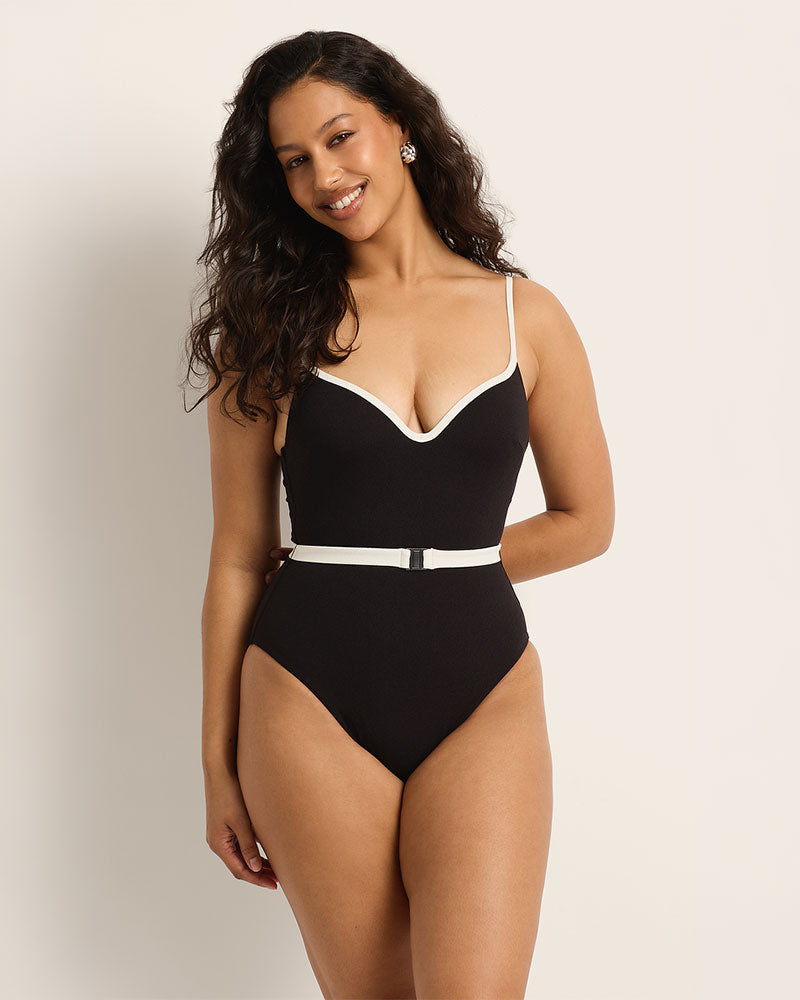 Woman wearing a supportive black swimsuit with white trim against a plain background