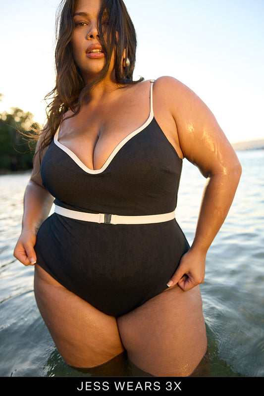 A woman stands confidently in shallow water wearing the Fearless au Grace High Rise One Piece, featuring moulded cups, white trim, and a belt. Text at the bottom reads: JESS WEARS 3X.