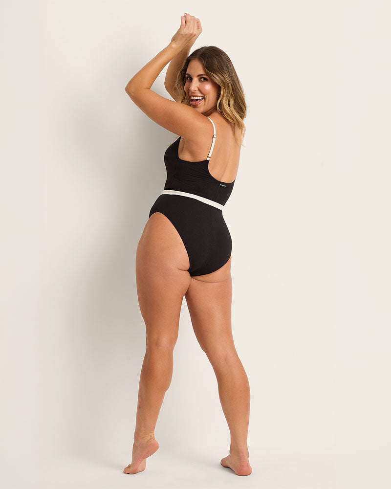 Woman wearing a supportive black swimsuit with white trim against a plain background