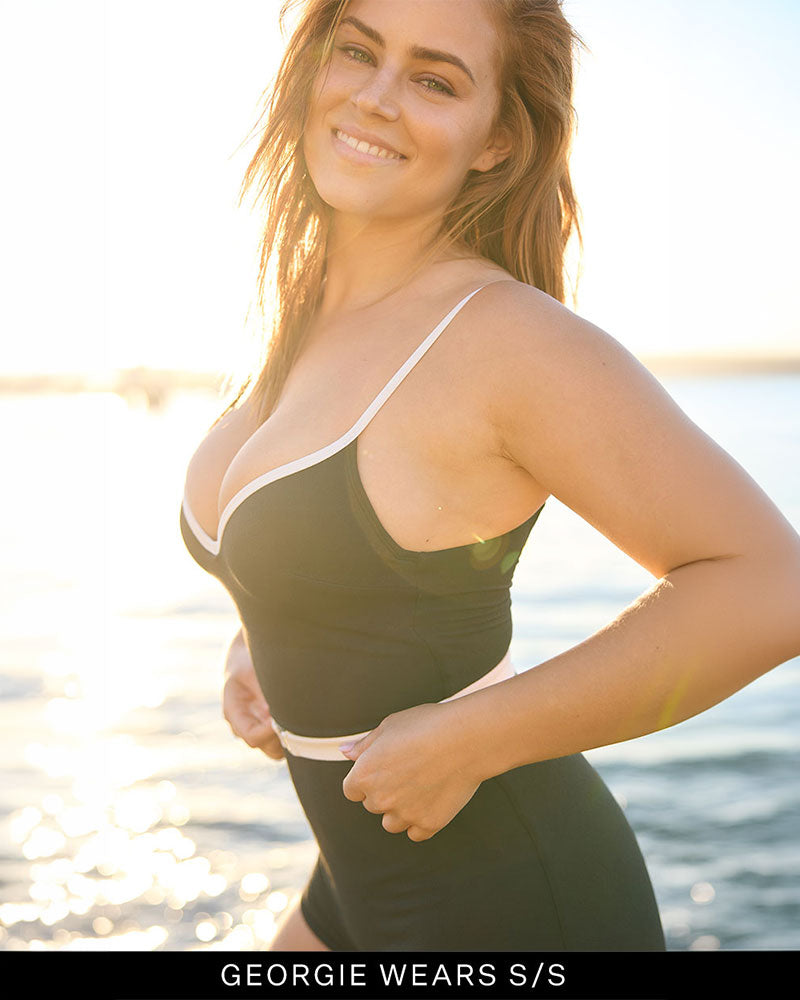 Woman in a supportive black and white swimsuit standing by a waterfront. 