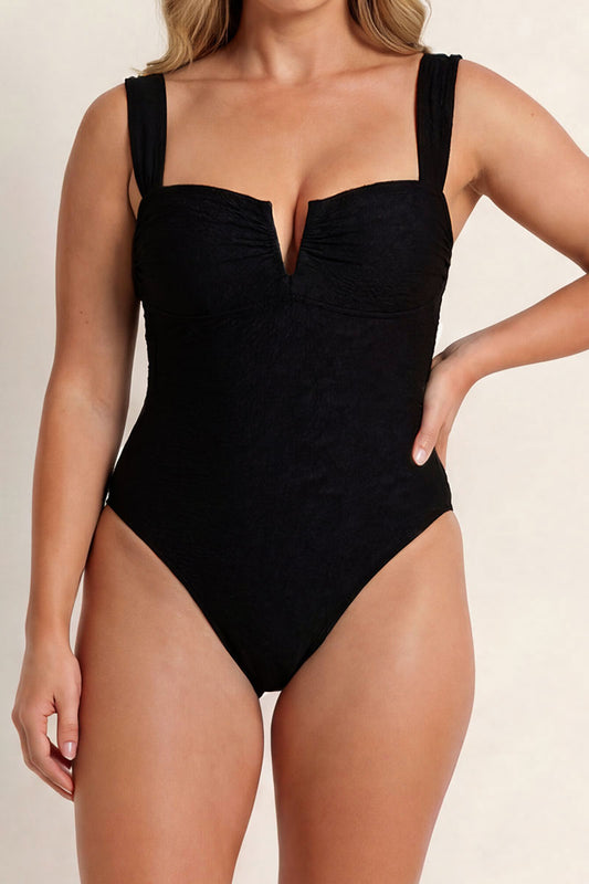 Black swimsuit worn by a model on a beige background
