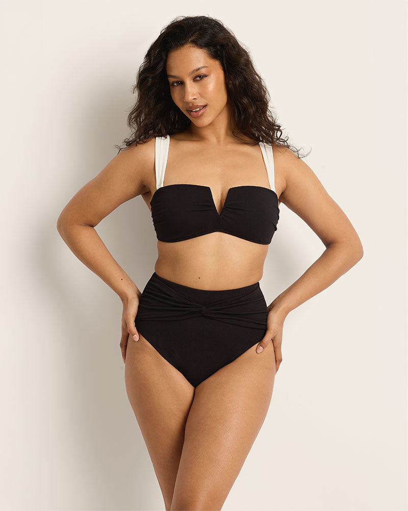 Woman wearing a black bikini with white straps against a plain background