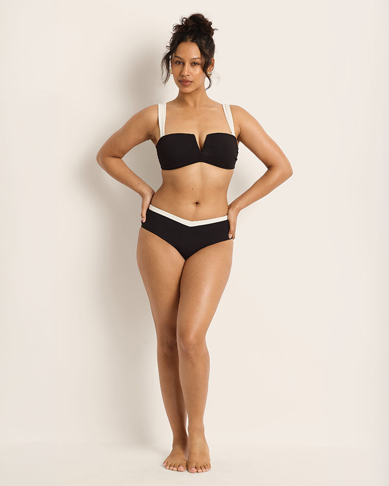 Woman wearing a black bikini with white straps against a plain background