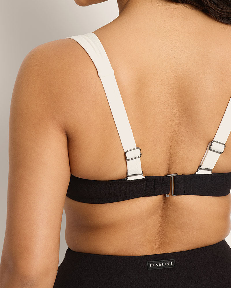 A woman stands with her back to camera, wearing a black and white bikini with Fearless logo on the back.