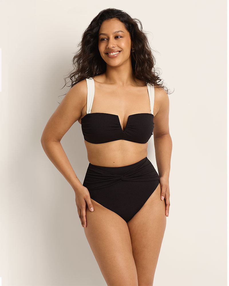 Woman wearing a black bikini with white straps against a plain background