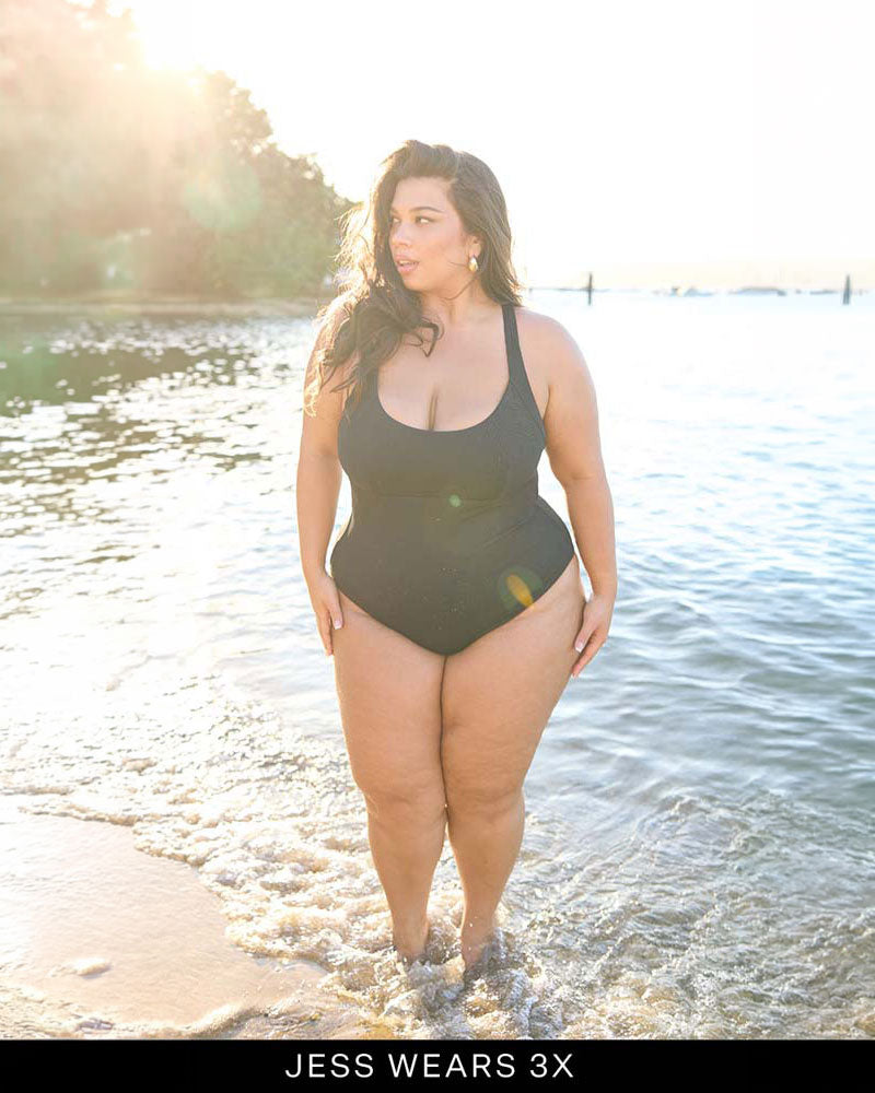 Woman wearing a black swimsuit standing in water with trees in the background.