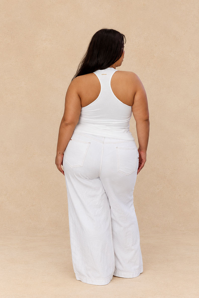 A woman shown from the back wearing a white sleeveless racerback top and matching white wide-leg pants, standing against a plain beige studio backdrop.