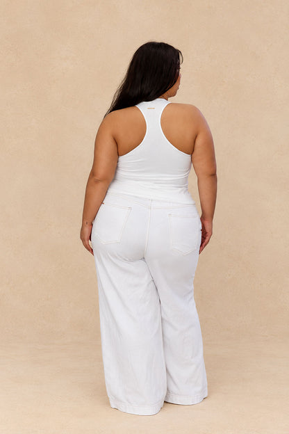 A woman shown from the back wearing a white sleeveless racerback top and matching white wide-leg pants, standing against a plain beige studio backdrop.