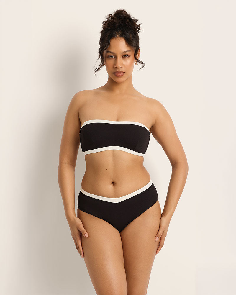 Woman wearing a black and white strapless bikini against a plain background