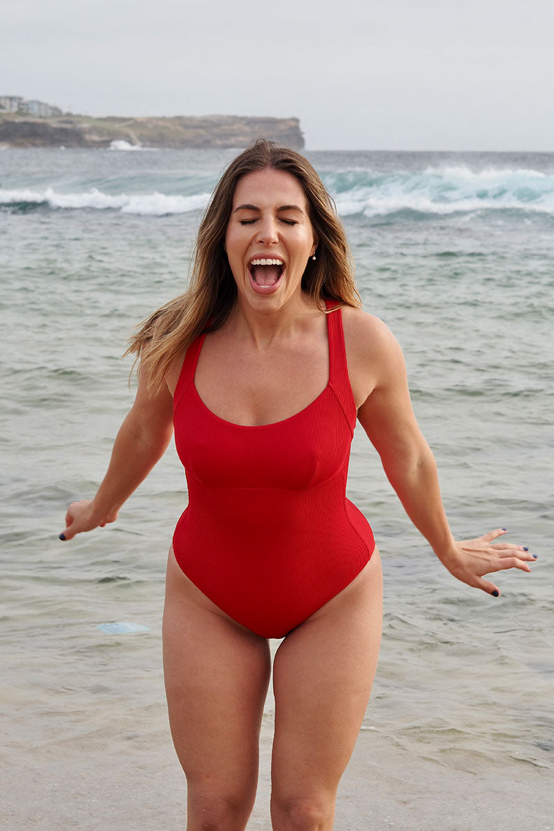 Woman in a red swimsuit standing on a beach with ocean waves in the background