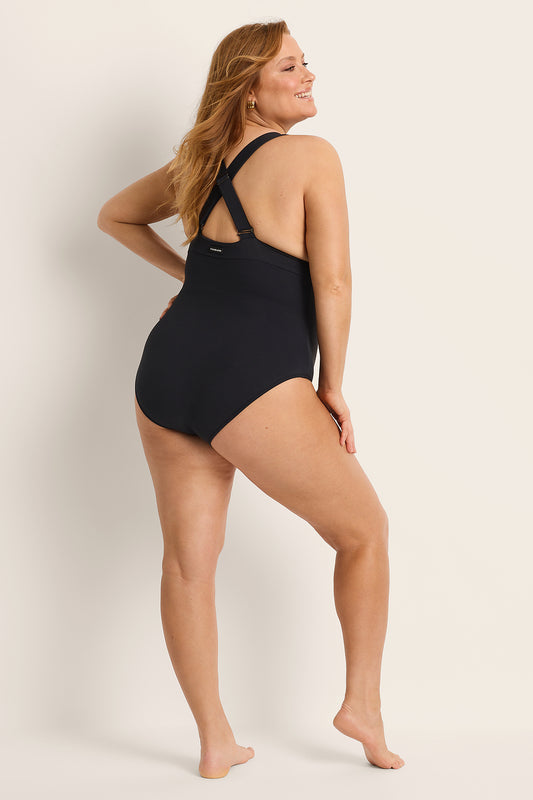 Woman wearing a supportive bust black one-piece swimsuit against a plain background.