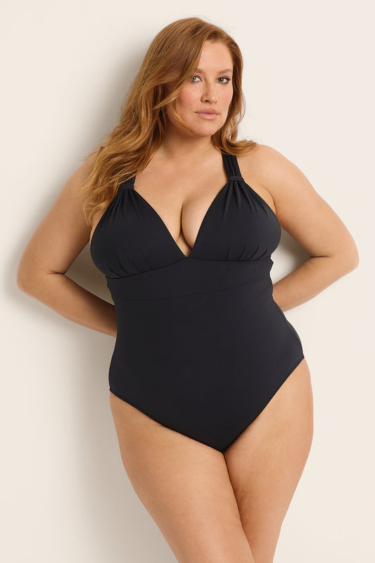 Woman wearing a supportive bust black one-piece swimsuit against a plain background.