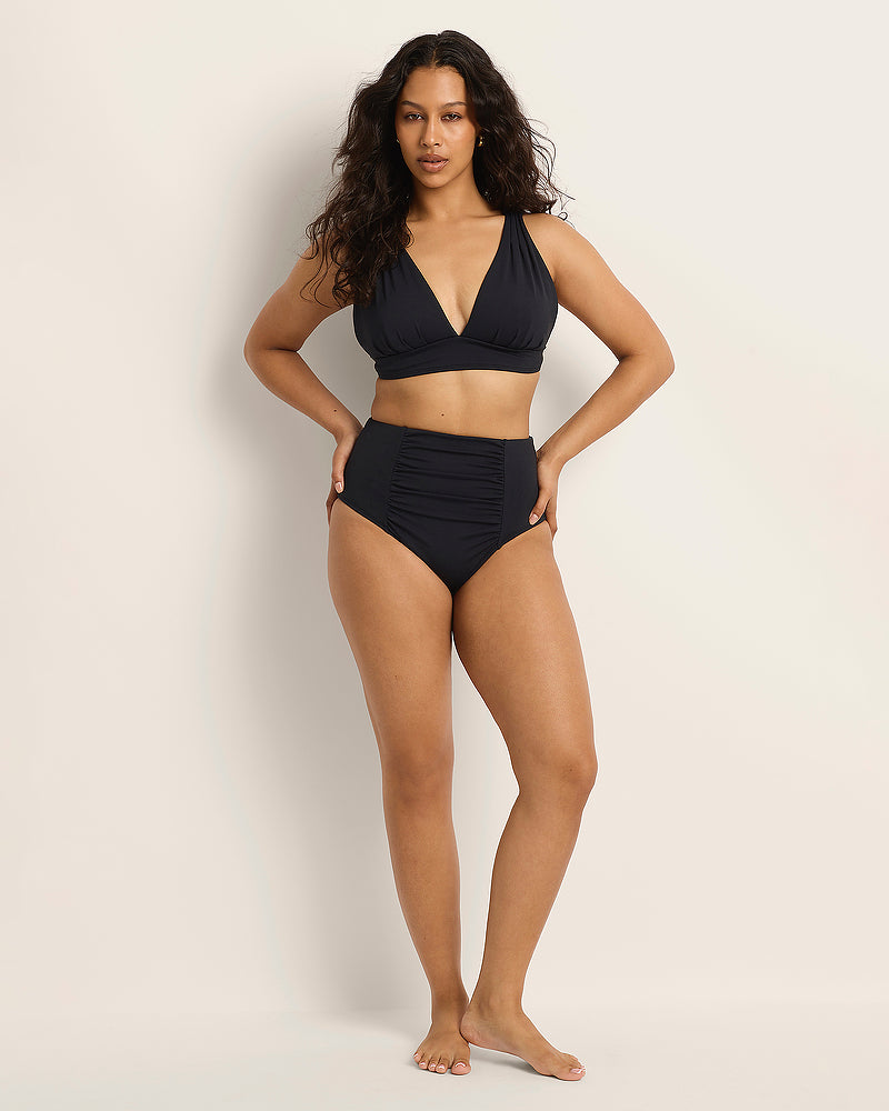 Woman wearing a Fearless supportive bust and high waist black bikini against a plain background.
